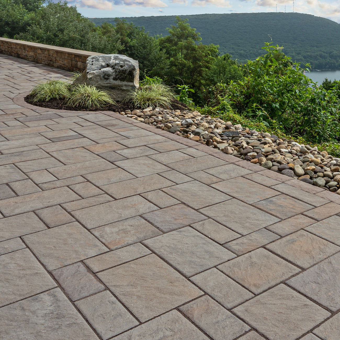 Edge of a patio installed with Trilogy+ Textured Pavers and a rock bed with a boulder.