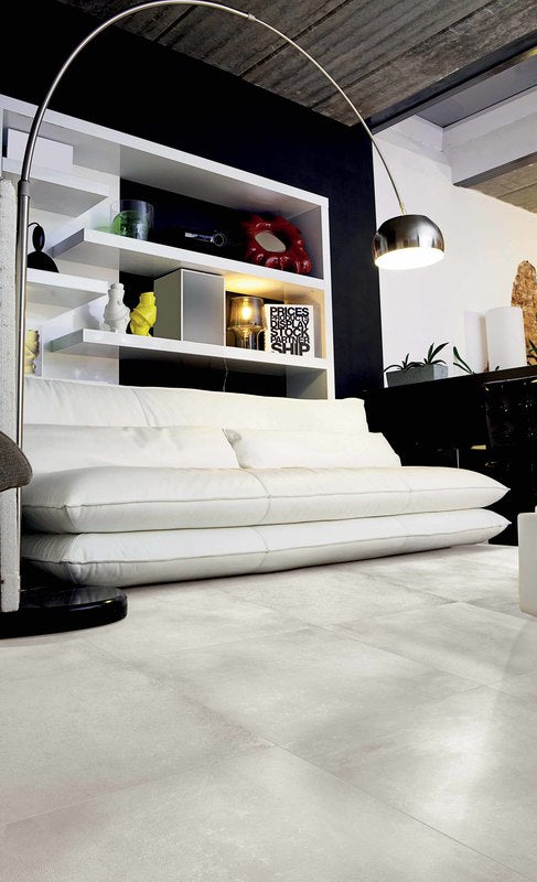 Living area featuring shelving and a large white couch. with basic grey porcelain tiles installed on the floor.