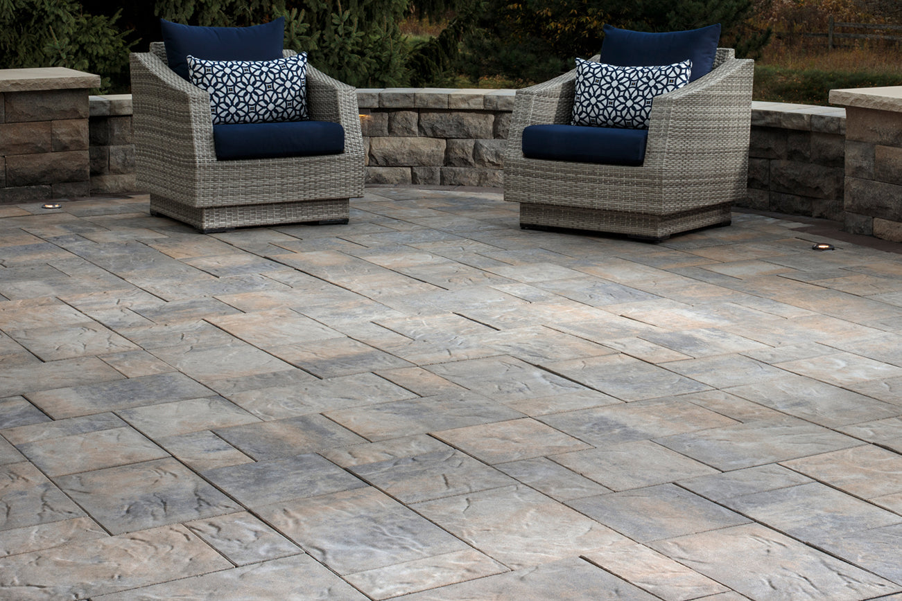 Large patio made with Origin Large Paver Set with a retaining wall and two patio chairs.