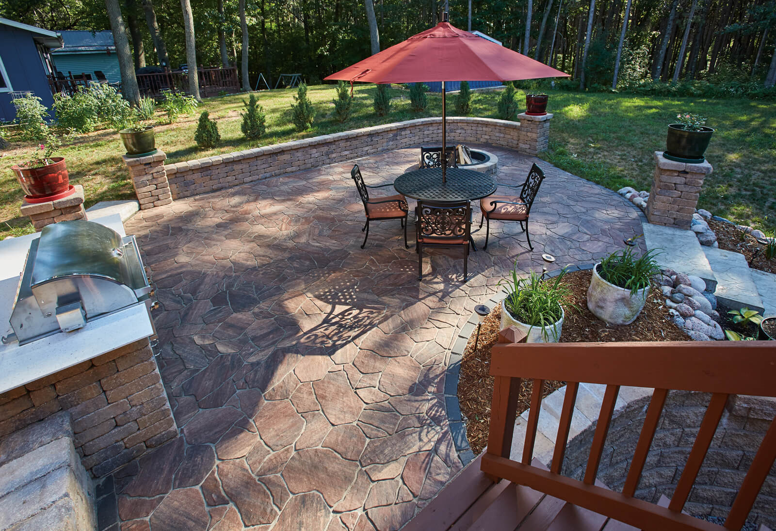 Patio made with Destination Pavers with outdoor kitchen, seating area, retaining wall and greenery.