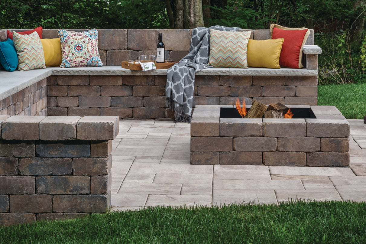 Back yard fire pit area on a patio with a retaining wall bench, pillows, blankets, and wine.