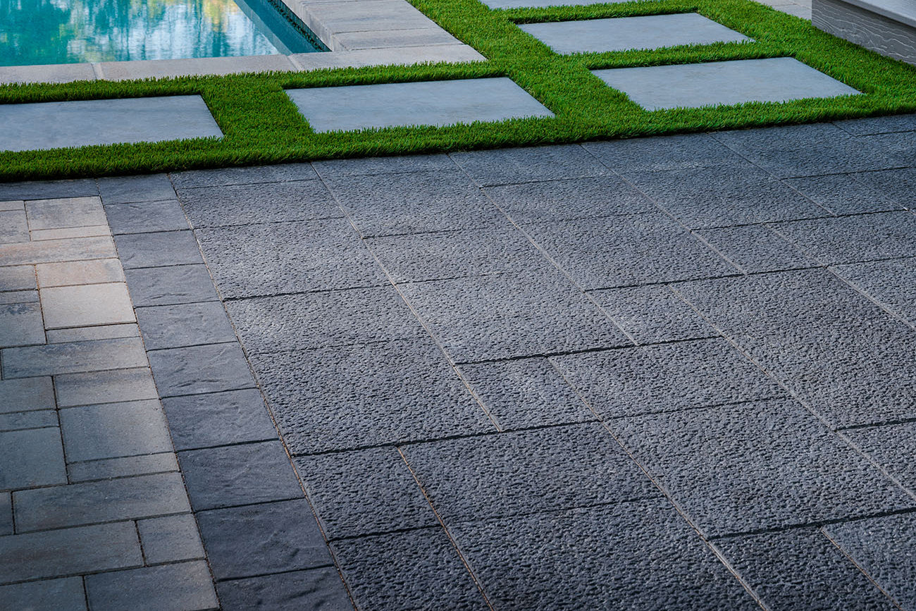 Patio made with basalt pavers with a pool in the background.
