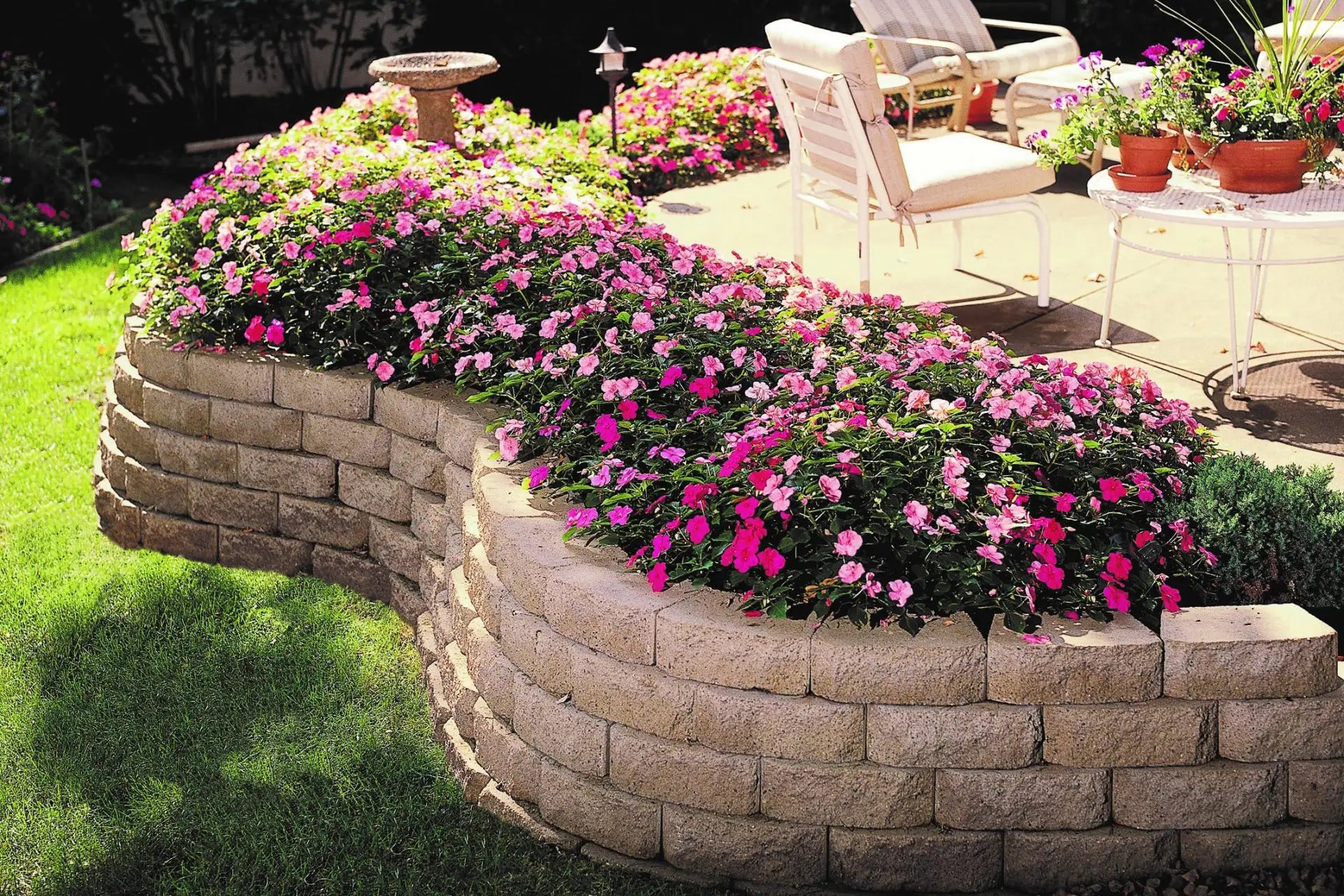 Retaining wall system made with Windsor Wall Blocks retaining a flower bed with pink and red flowers.