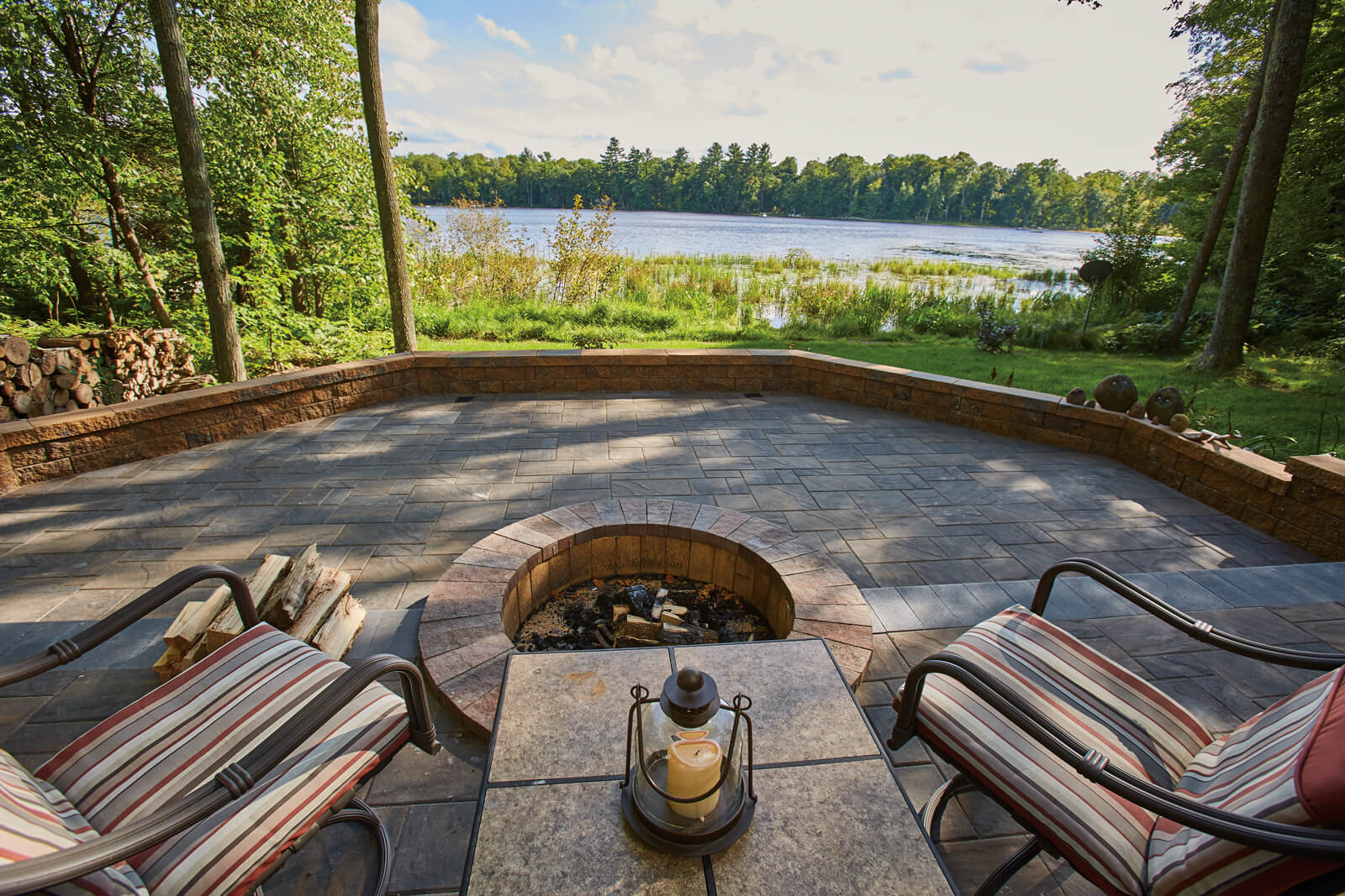 Water front patio made with Tranquility Paver Set with a firepit and seating looking out onto the water.